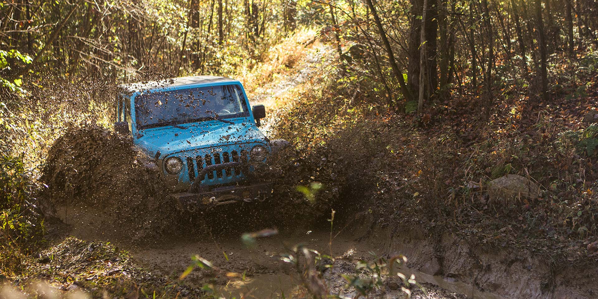 blue jeep driving into mud through a forest on an off-roading adventure